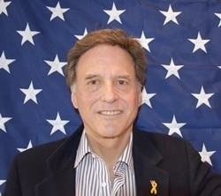 Man smiling in front of an American flag backdrop.