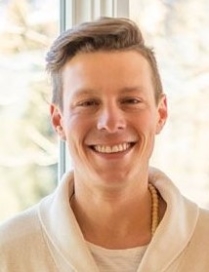 A smiling young man with short hair in a light-colored shirt.