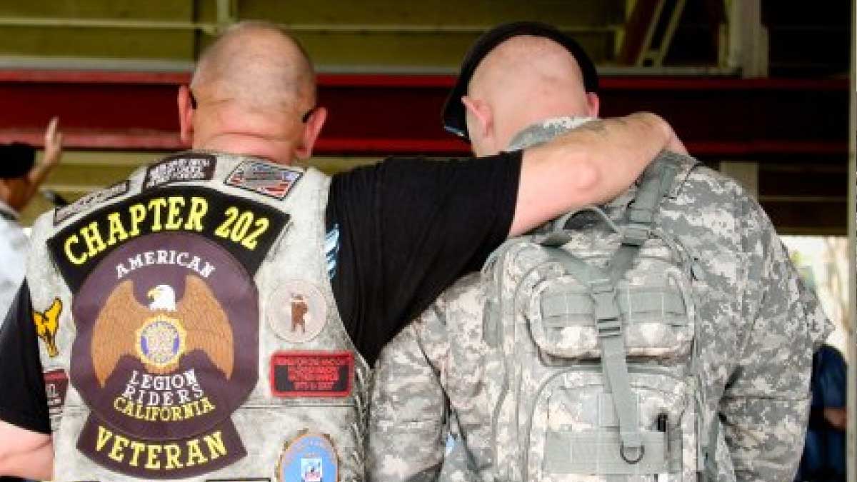Two men, one in military uniform, with arms around each other showing camaraderie.
