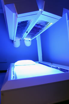 A modern UV light therapy bed glowing blue in a clinical room.